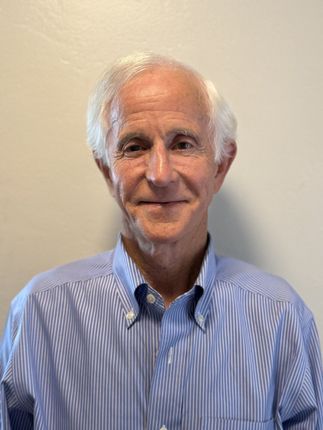 Portrait of a smiling man in a blue striped shirt against a plain beige wall