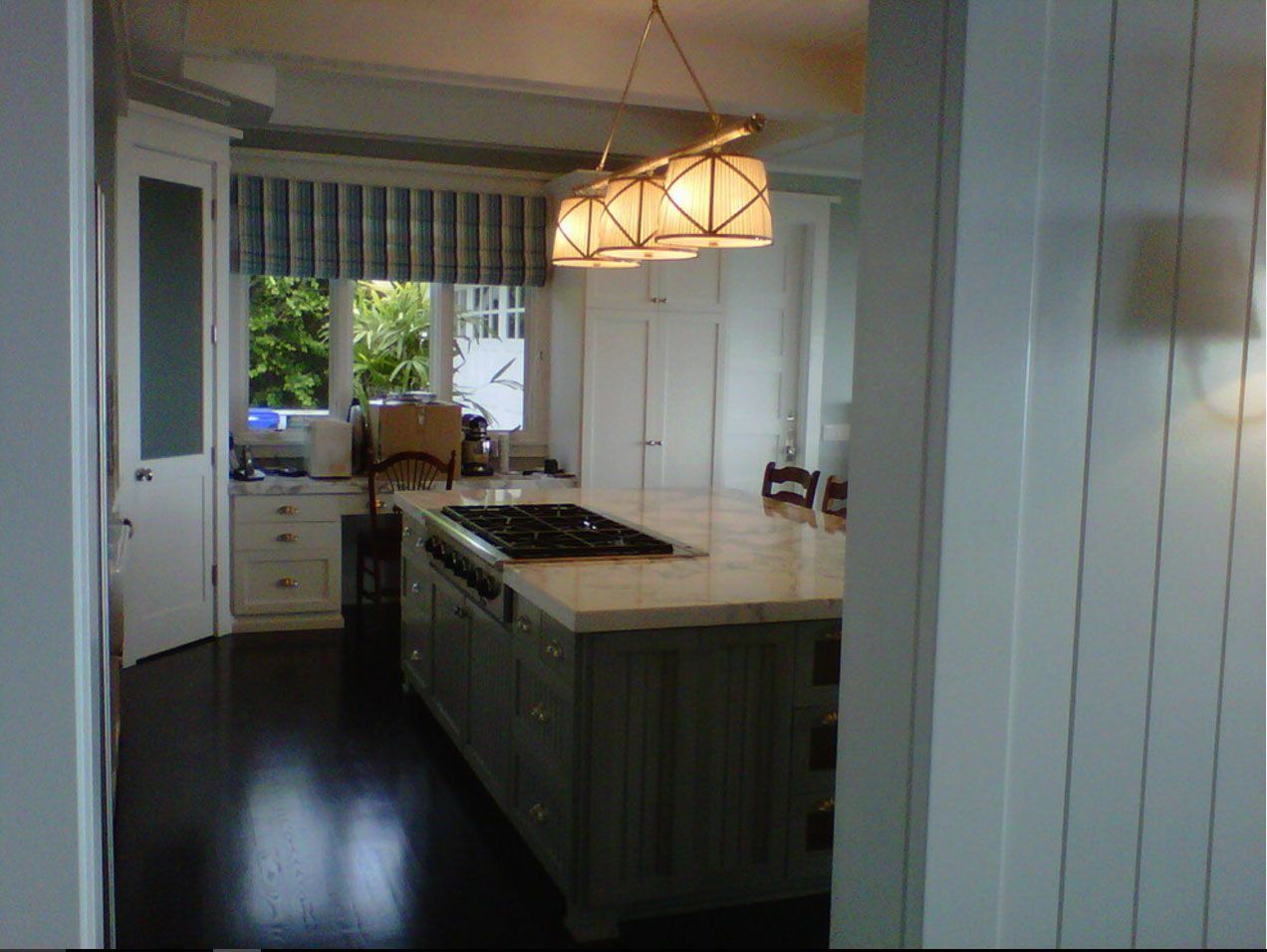 Bright kitchen with white cabinets, dark floor, island, and pendant light by a window