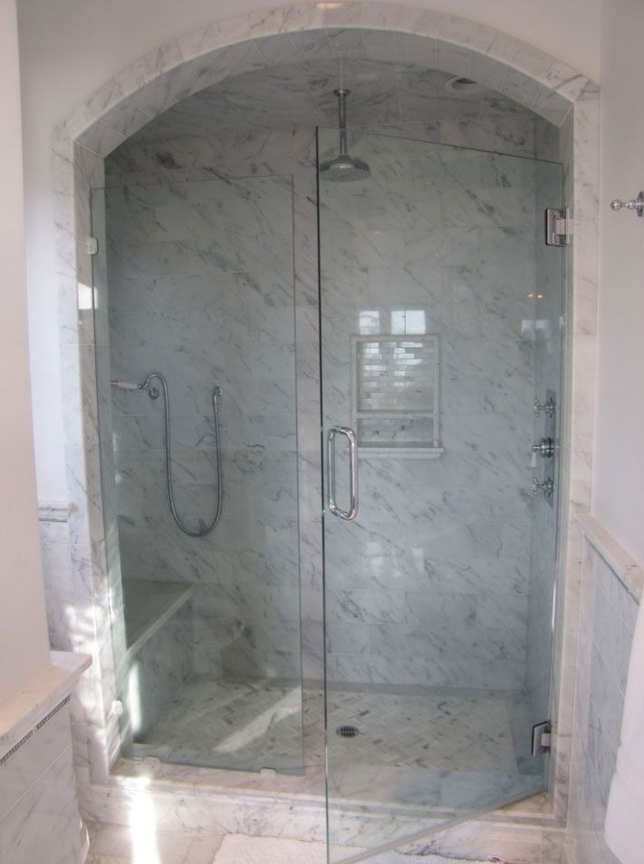 Marble walk-in shower with glass doors, built-in bench, and handheld showerhead under an arched opening