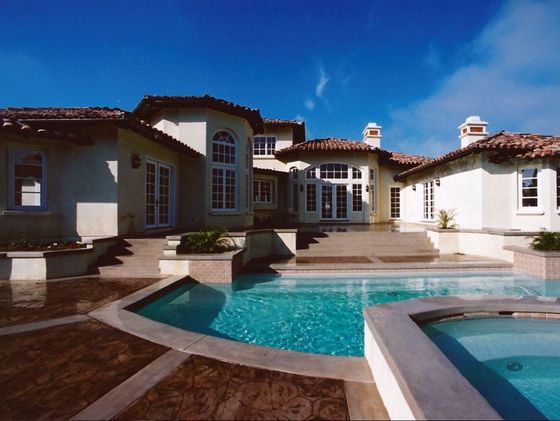 Luxury house with a tiled patio and turquoise pool under a clear blue sky