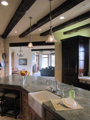 Modern kitchen with a large island, pendant lights, dark wood beams, and a sink in the foreground