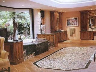 Empty beige bedroom with hardwood floor, ceiling fan, closet doors, and two windows.