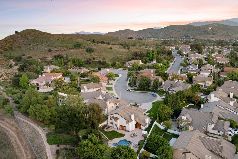 Aerial view of a suburban hillside neighborhood at sunset with winding streets and green hills.