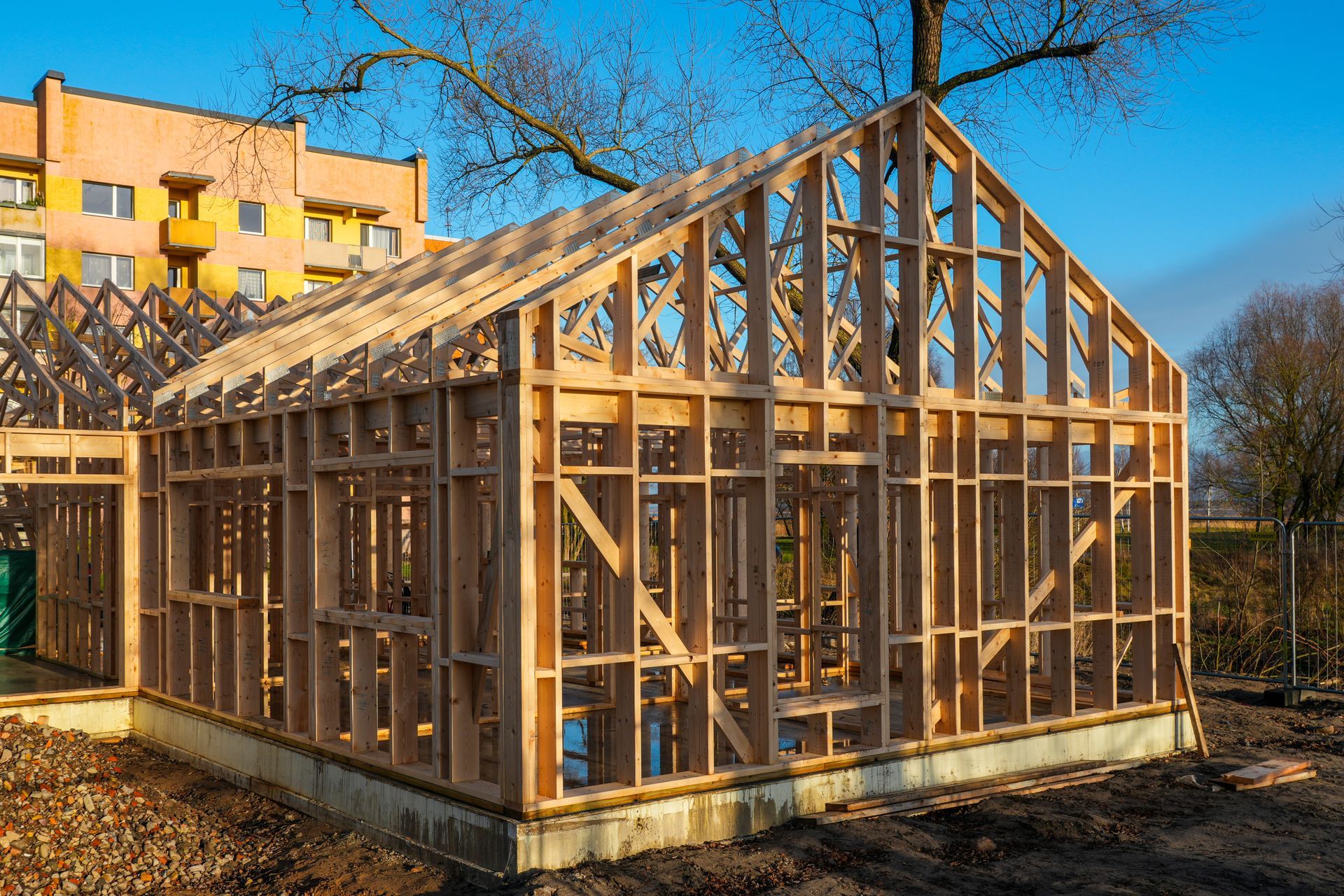 Wood-framed house under construction with exposed roof trusses in a sunny outdoor setting