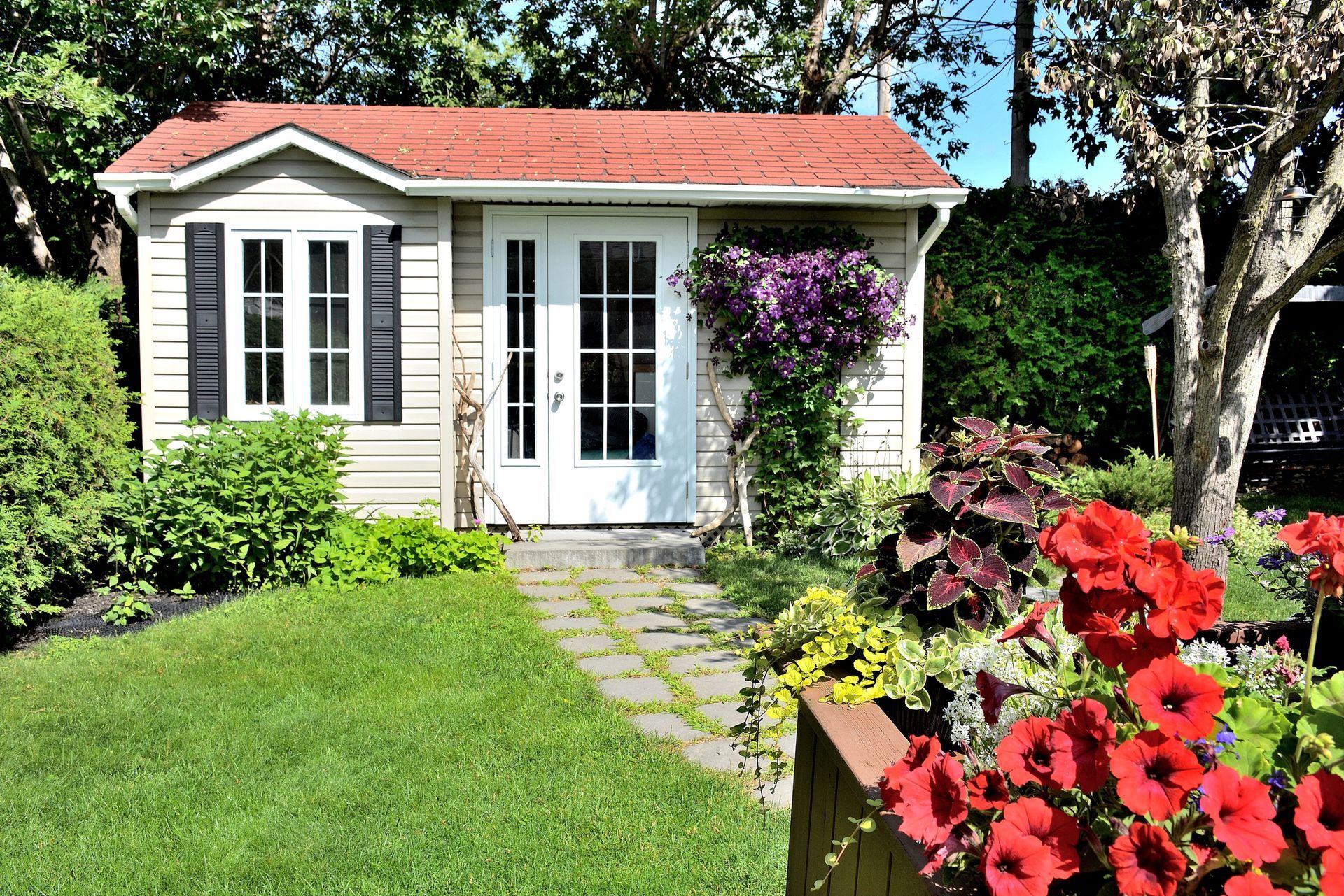 A small house with a red roof is surrounded by flowers and trees.