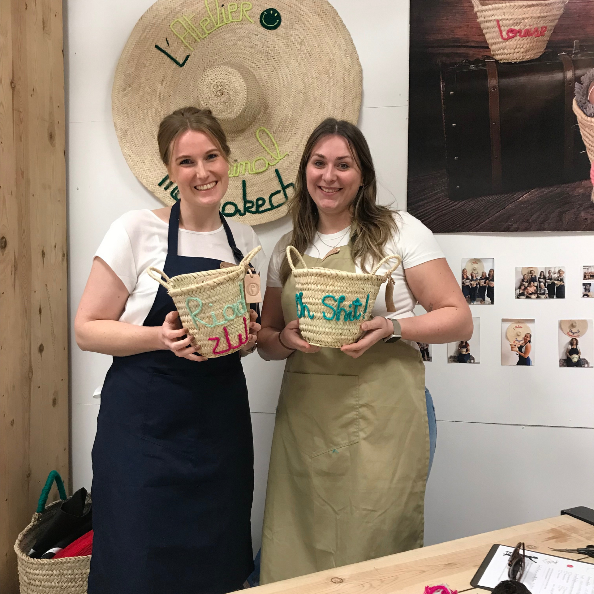 Deux femmes souriantes présentent des paniers brodés colorés dans un atelier à Marrakech. 