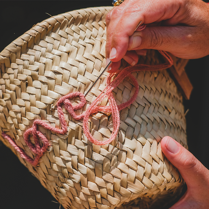 Personnalisation d'un panier en feuille de palmier avec une broderie 'Love' lors de l'atelier de bro