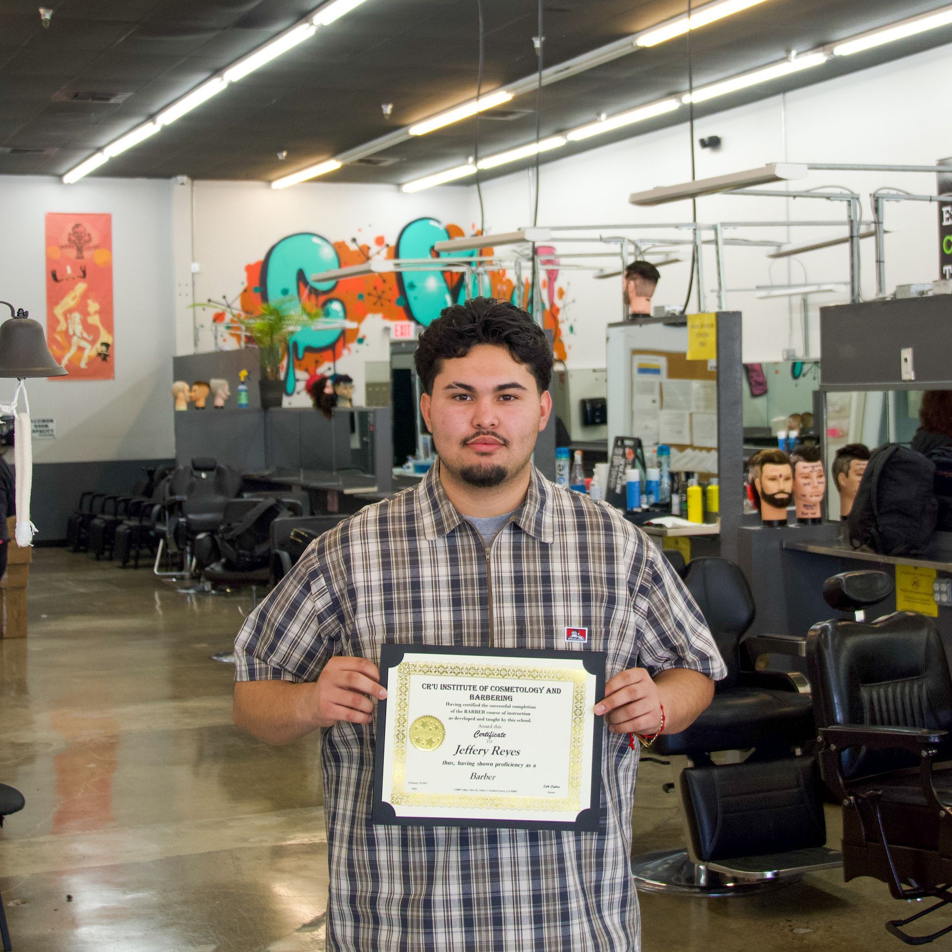 Person holding a certificate in a barbershop with colorful wall art in the background