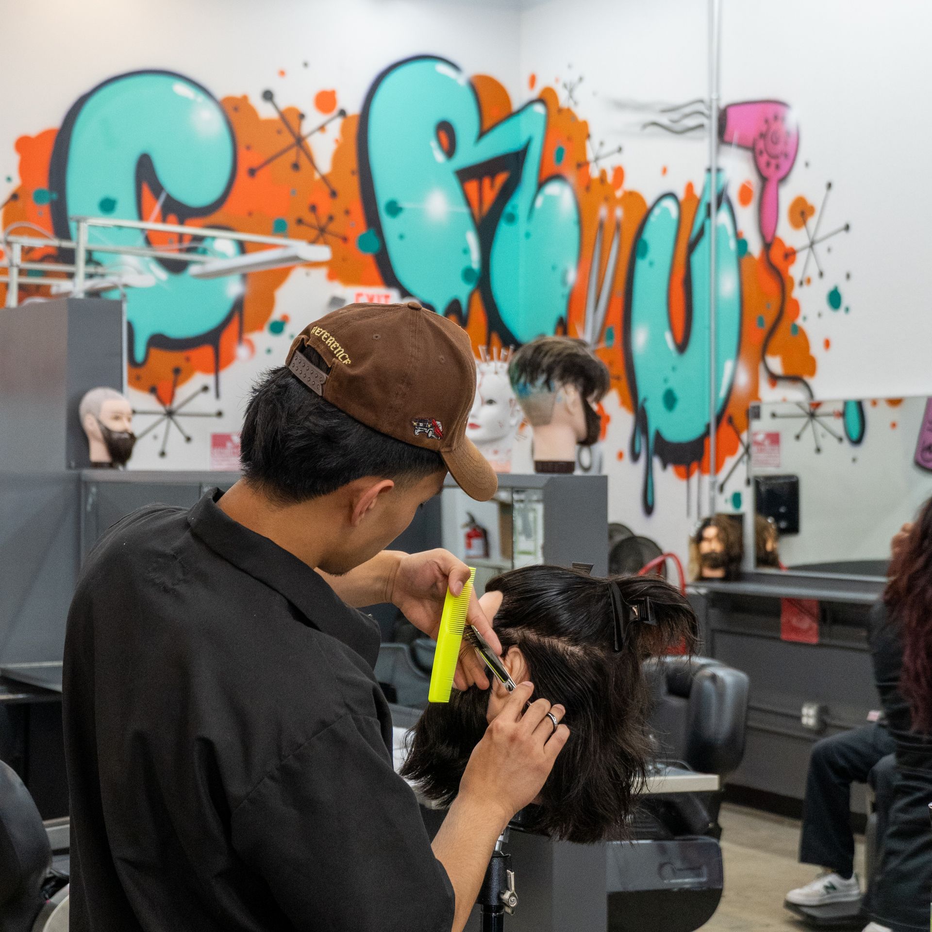 Hairdresser cutting a client’s hair in a barbershop with turquoise graffiti wall art.