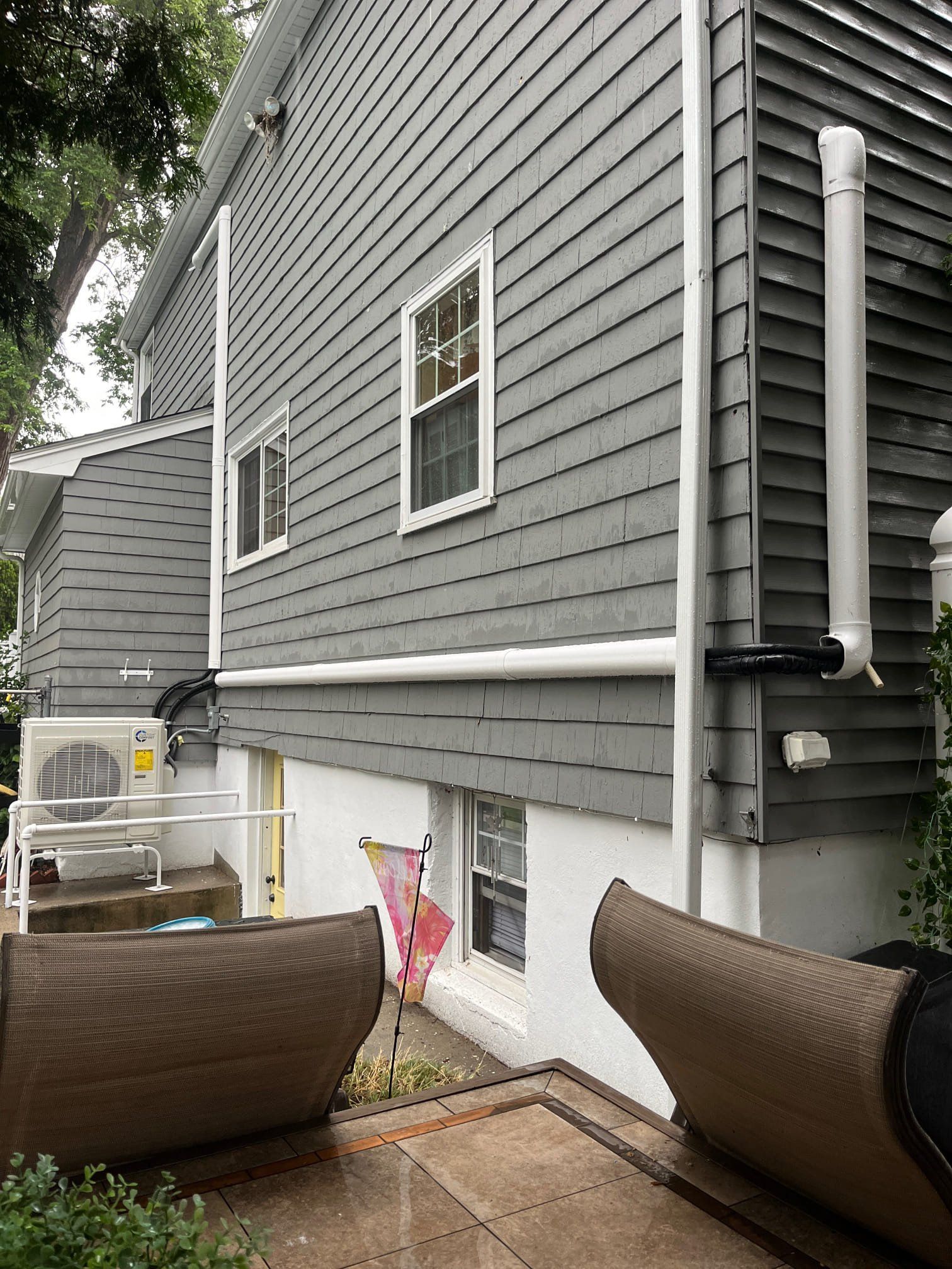 Gray siding on a two-story building with white trim and a white pipe running down the side.
