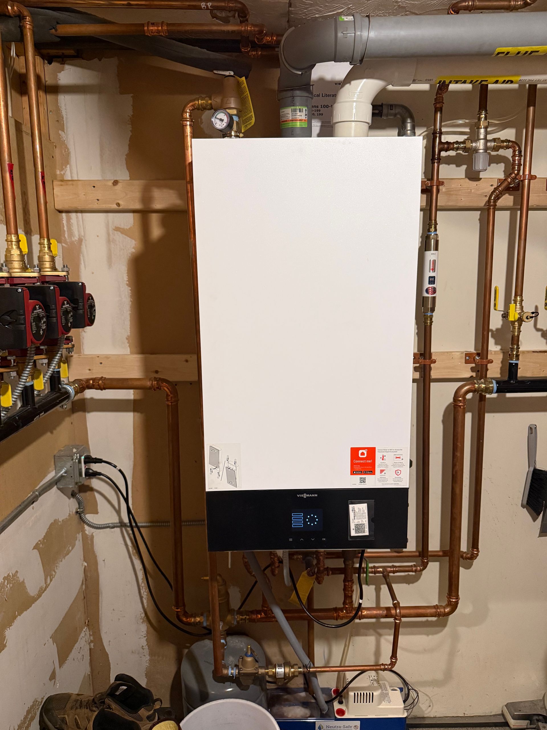 White wall-mounted boiler with copper pipes in a basement setting.