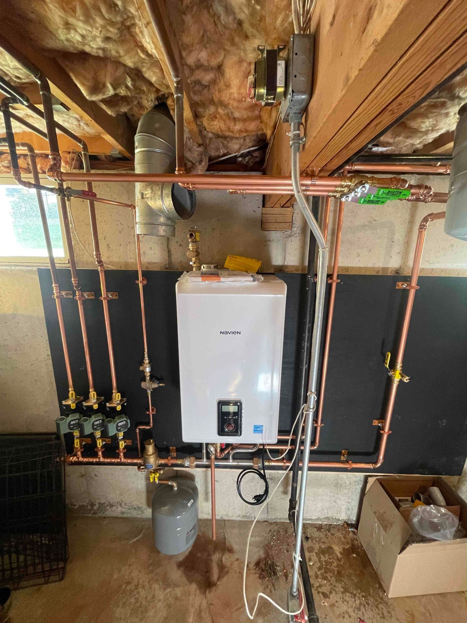 Copper pipes and a white water heater installed on a basement wall.