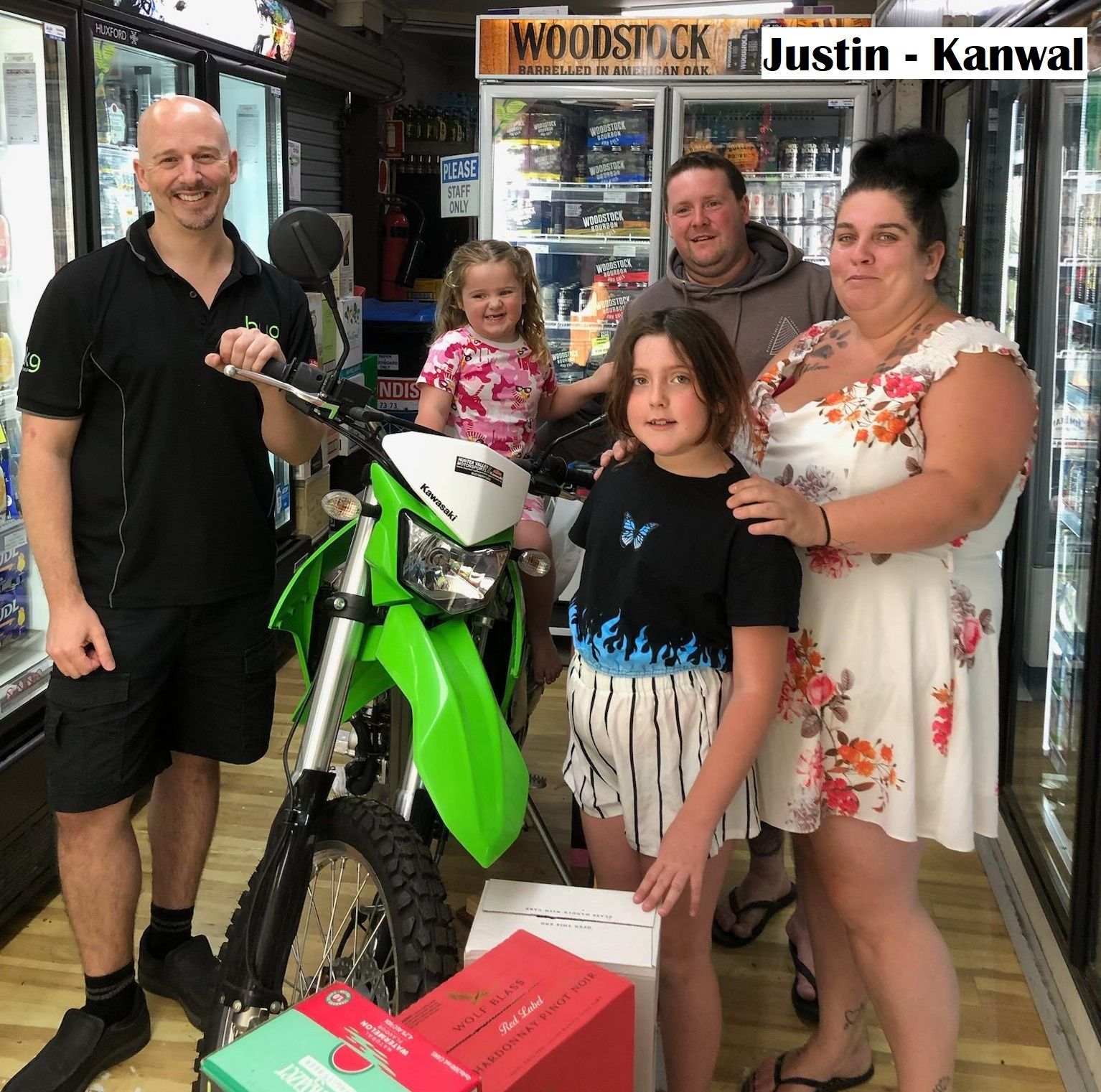 Man holding green motorcycle with family and employee in a store.