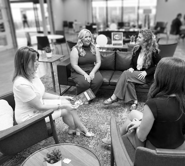 Four people seated in a lounge, chatting in a circle around a low table.