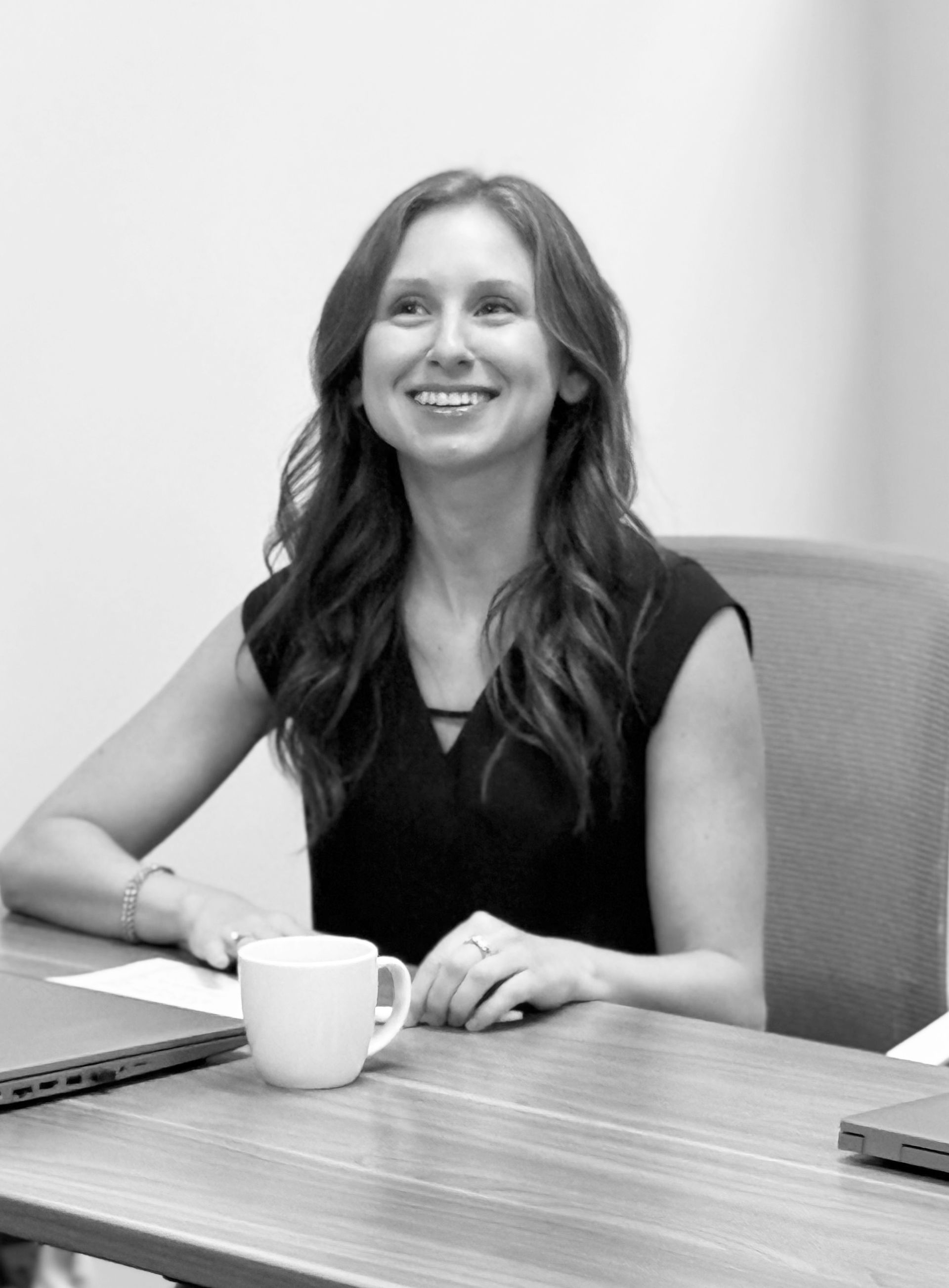 Woman smiling at a table with a laptop and coffee mug in an office meeting room