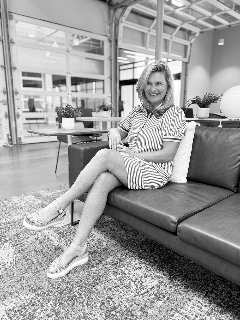 Woman sitting on a couch in a bright modern lounge, smiling and holding a cup.