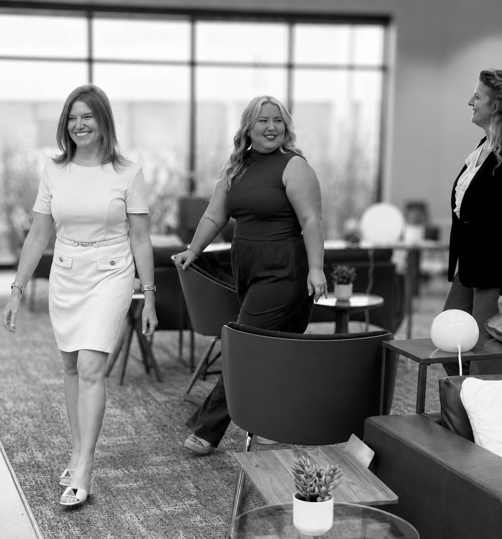 Three women walking through a modern lounge area, smiling and carrying drinks.
