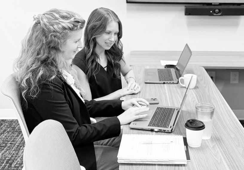 Two people working on laptops at a conference table in a meeting room