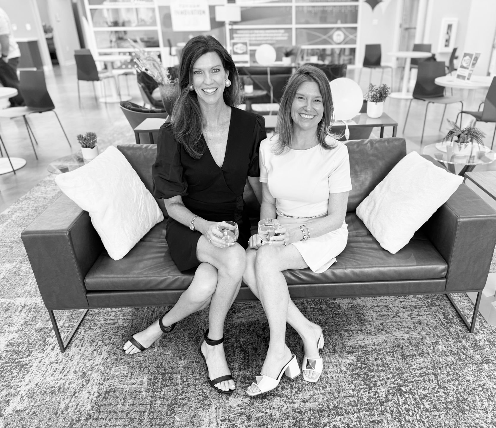 Two women sitting on a couch in a modern lounge, smiling at the camera.