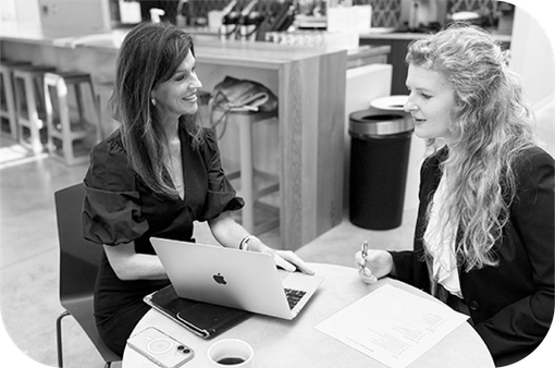 Two women talking at a café table with a laptop and papers