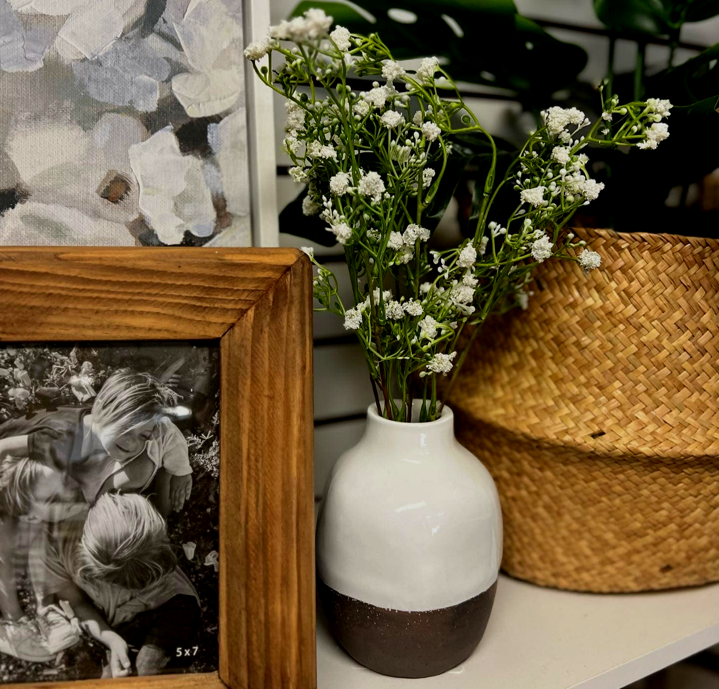 A vase filled with white flowers is sitting on a shelf next to a picture frame.