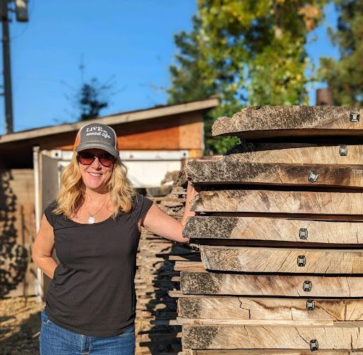 A woman is standing next to a pile of wood.