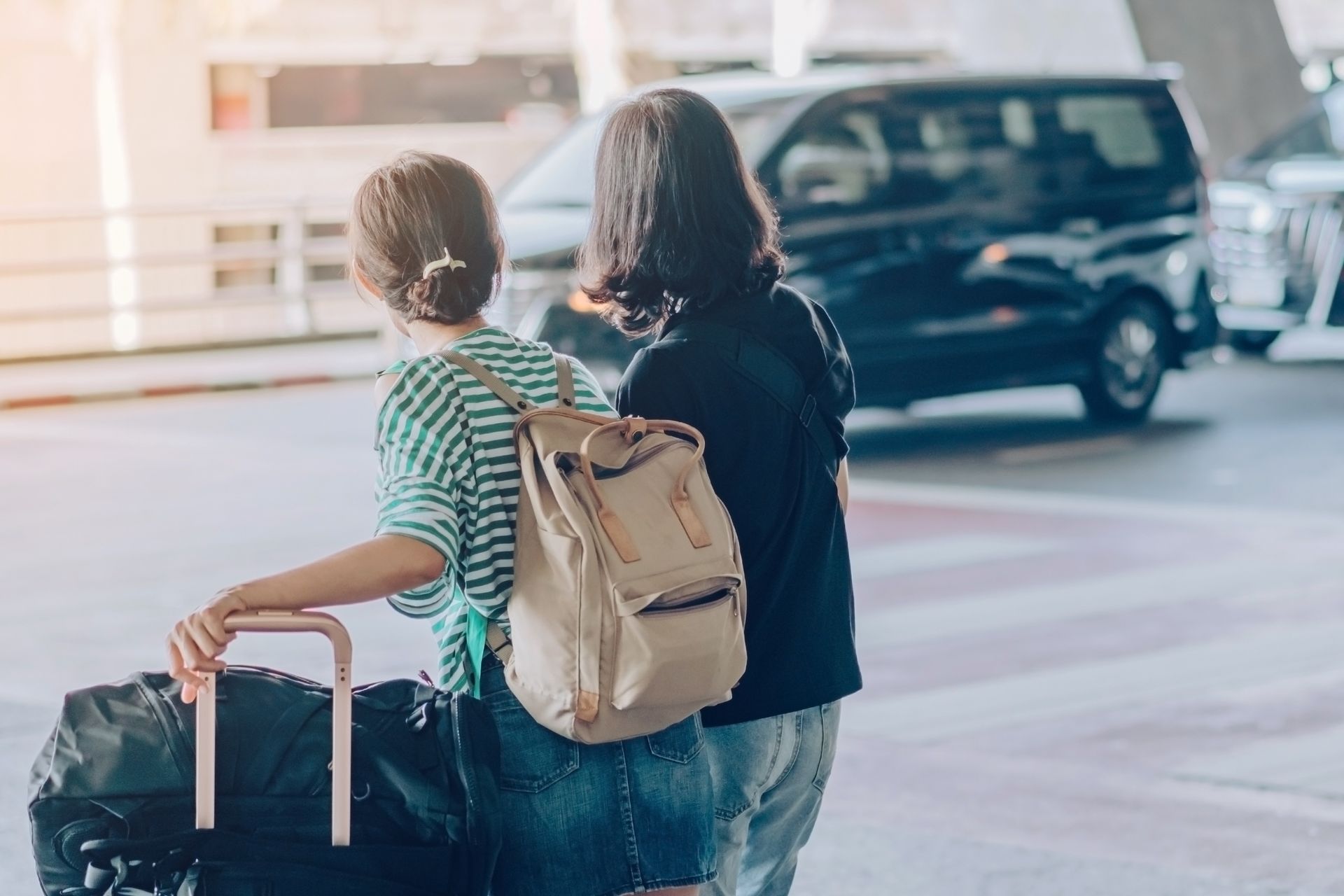 Two women are pushing a luggage cart at an airport.