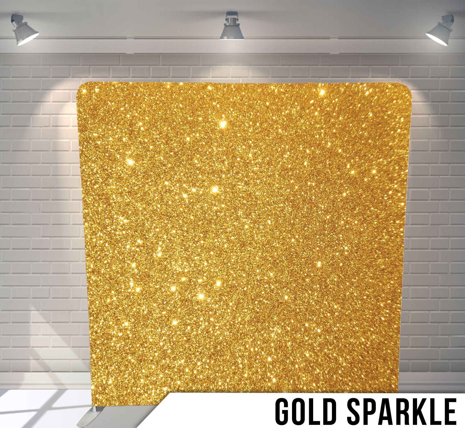 Gold glitter backdrop against a white brick wall, lit by spotlights.