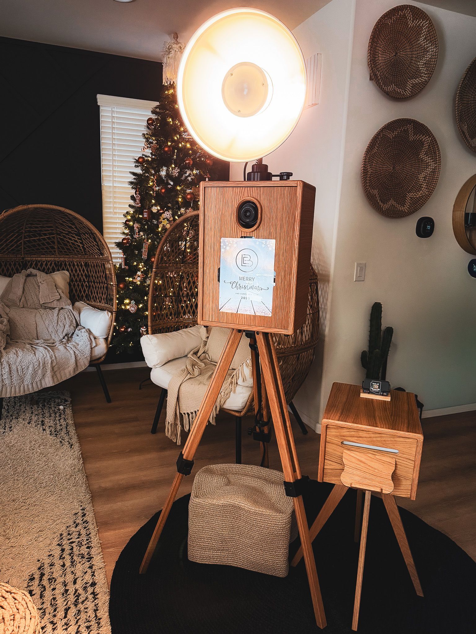 Wooden photo booth with large light, set up for an event, with Christmas tree and decor in the background.