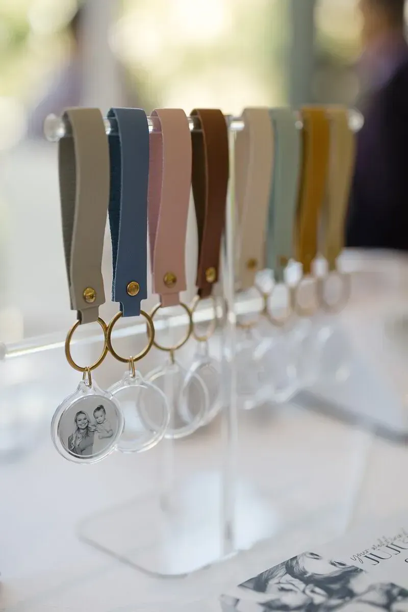 Keychains with leather straps in various colors displayed on a clear stand, one with a photo.