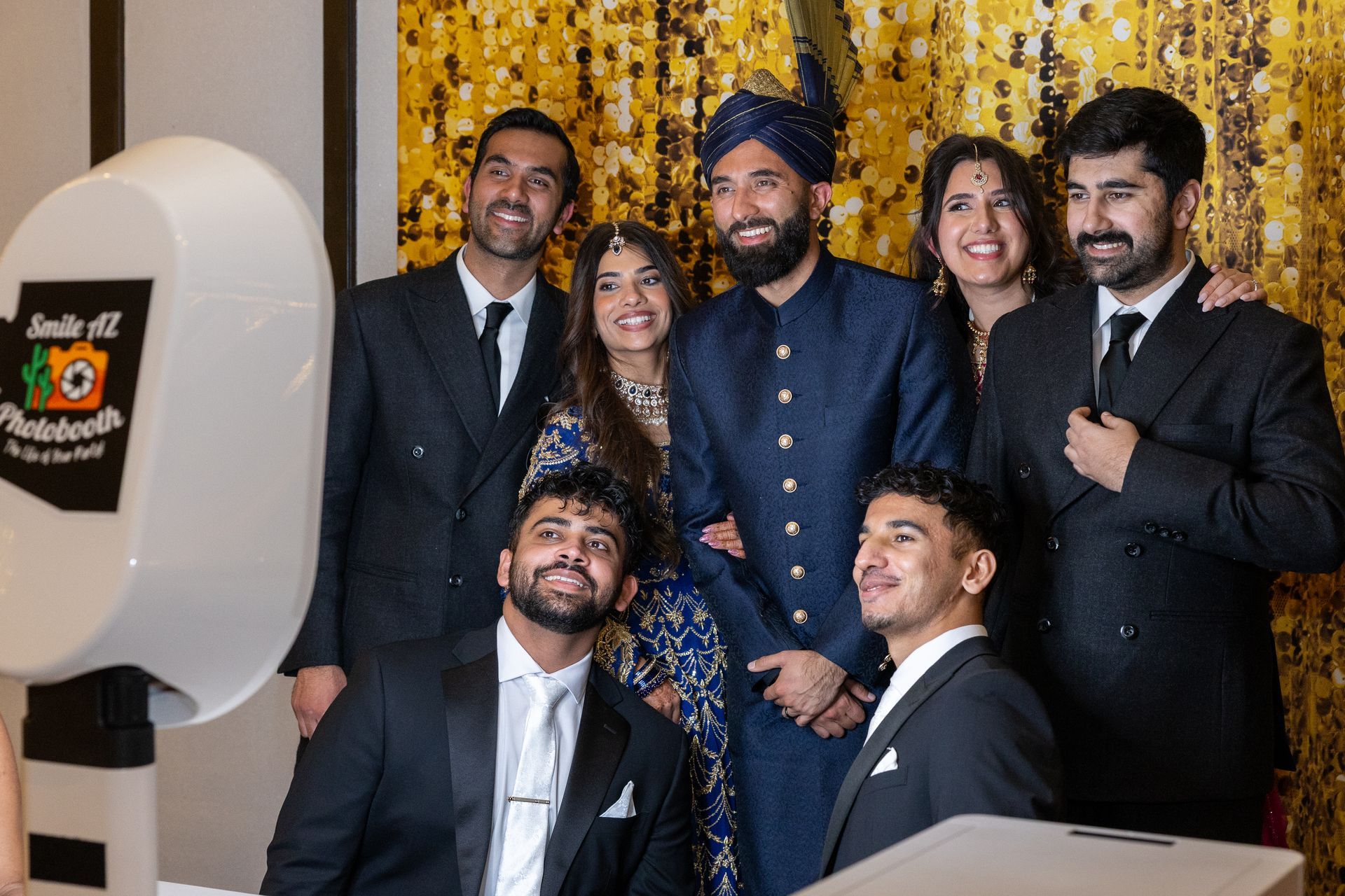 Group of people posing for a photo booth. Some are smiling; the setting has a gold backdrop.