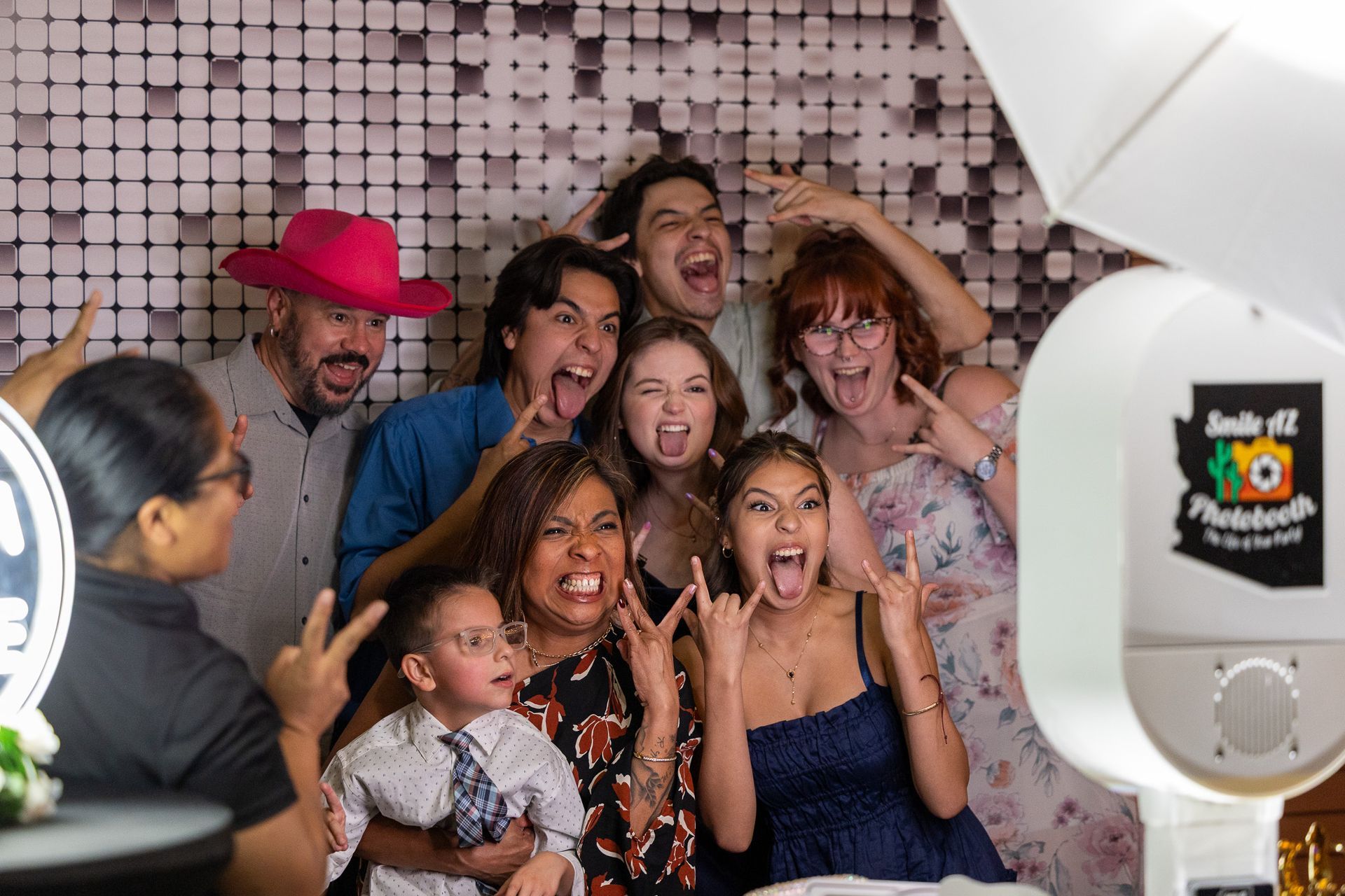 Group of people at a photo booth, making silly faces and gestures. White and silver backdrop.