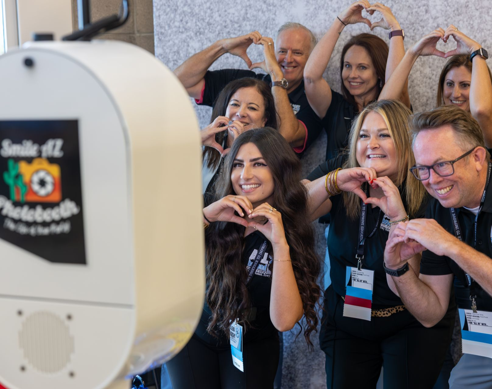 Group of people posing with hands in heart shapes next to a photo booth.