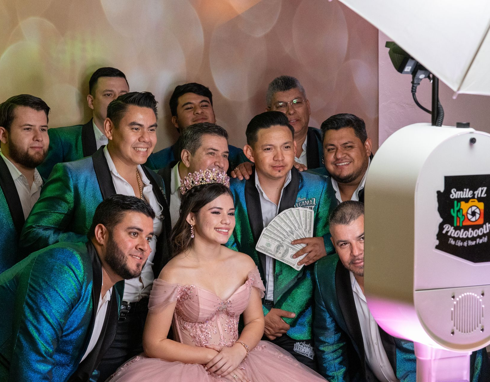 Group photo: a woman in a pink gown poses with men in teal jackets by a photo booth.