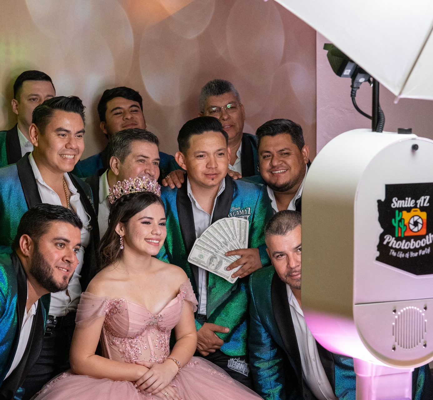 Group poses with a young person in a pink gown at a photo booth. Party setting.