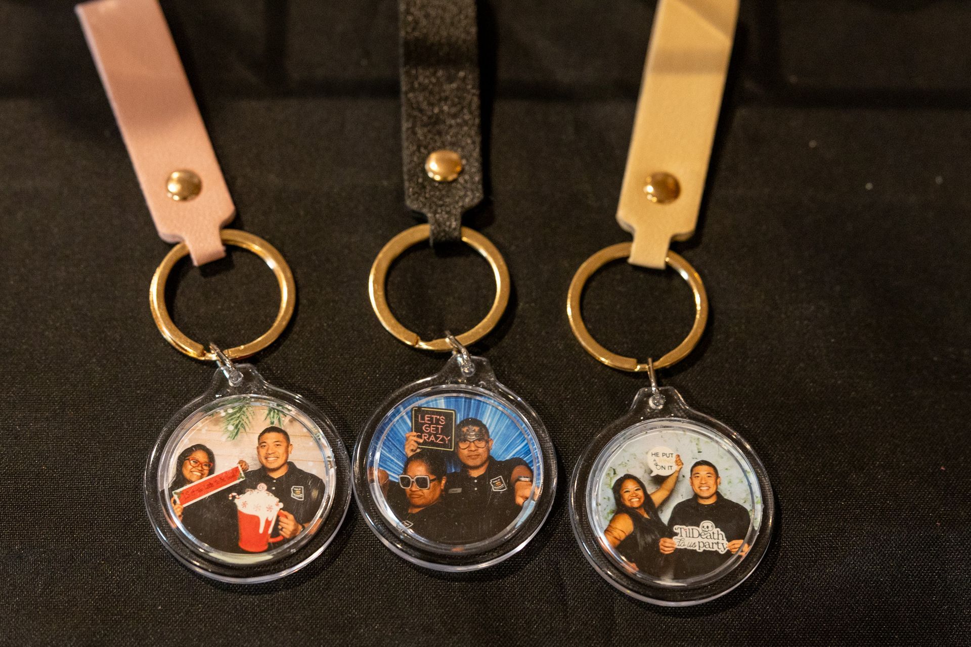 Three personalized keychains with photos, featuring pink, black, and tan straps, gold rings.