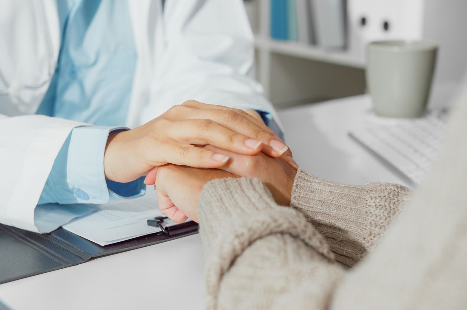 A doctor is holding a patient 's hand while sitting at a desk.