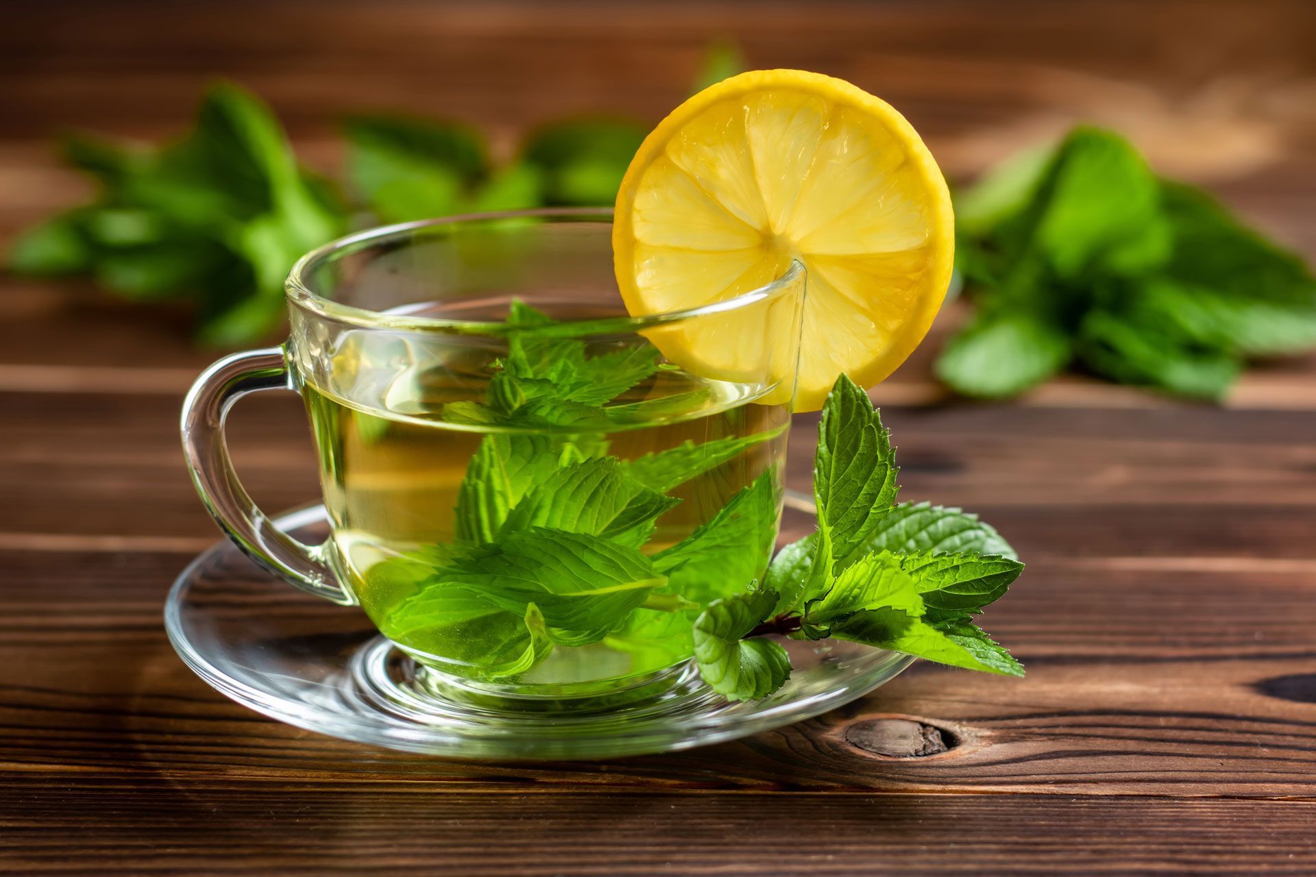A cup of mint tea with a slice of lemon on a wooden table.