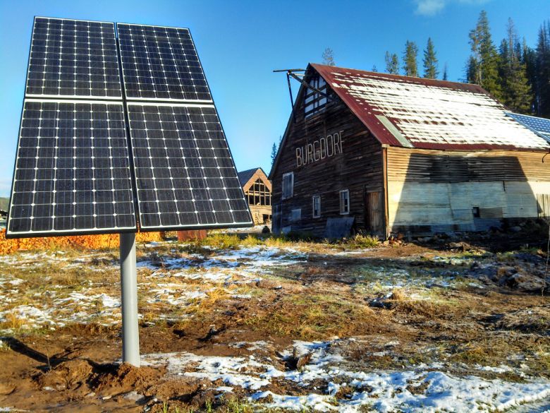 Five solar inverters mounted on a white wall under a blue sky. Gray conduit runs beneath them.