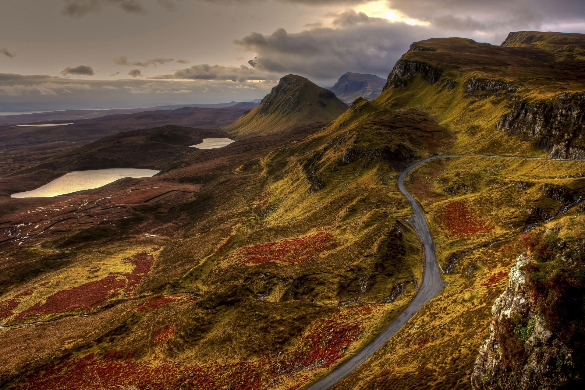 Winding road through Scottish mountains, lakes and low-lying moorland under a cloudy sky.
