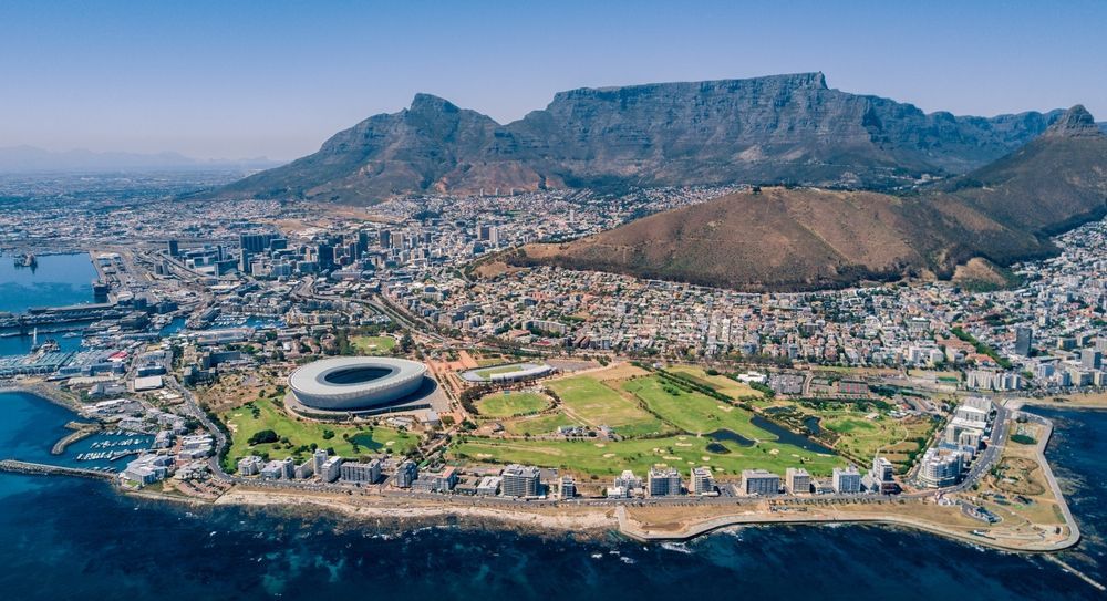 Aerial view of Cape Town, South Africa, with a stadium, golf course, and Table Mountain in the background.