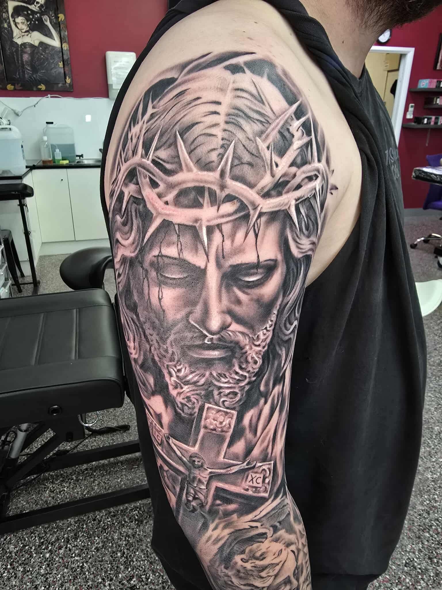 A Man's Arm Tattoo of Jesus Wearing a Crown of Thorns and a Cross — Redback !nk Tattoo Studio in Kawana, QLD