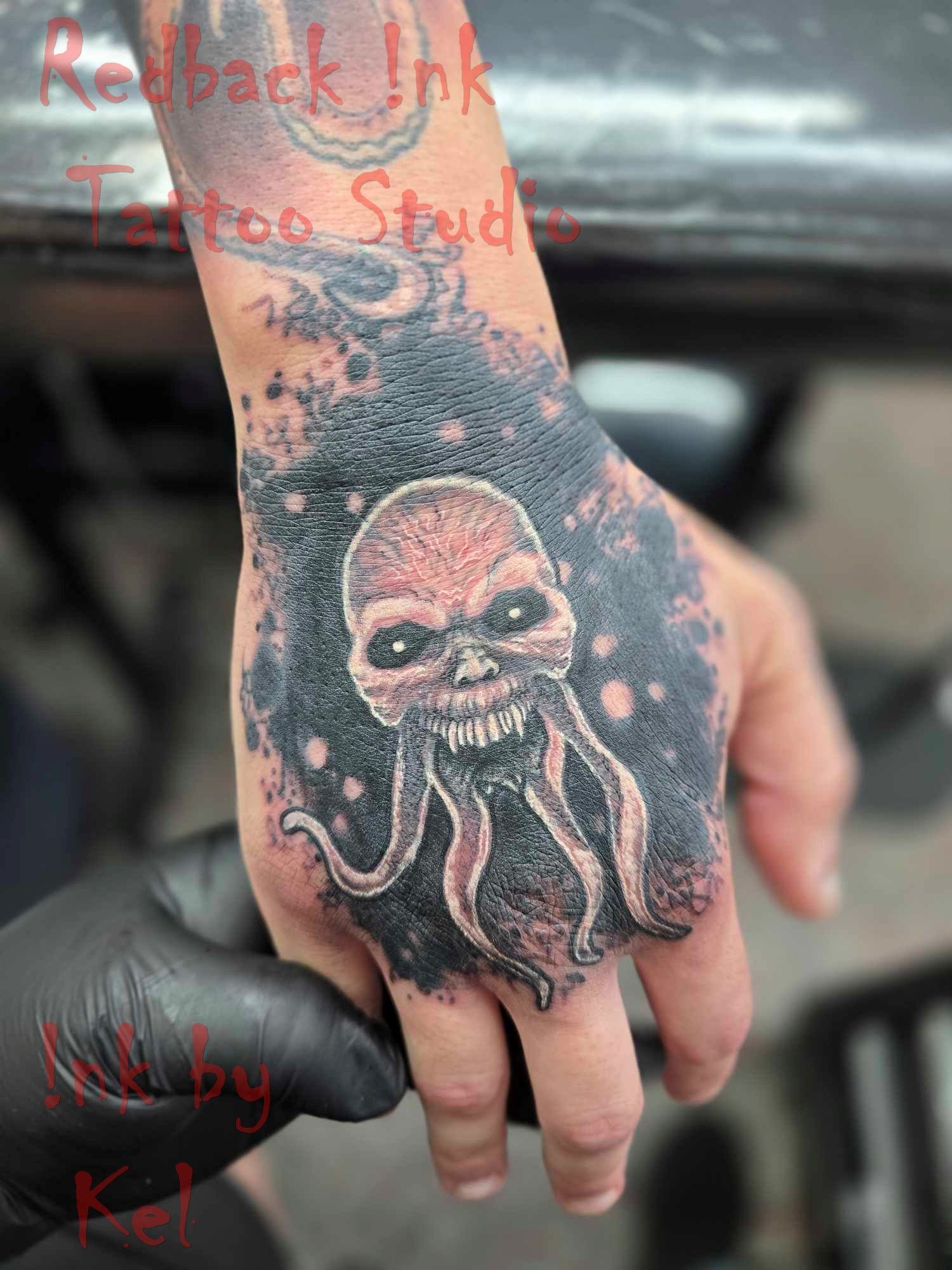 Tattoo on Hand: A Skull-like Creature With Tentacles, Surrounded by Black Ink — Redback !nk Tattoo Studio in Kawana, QLD