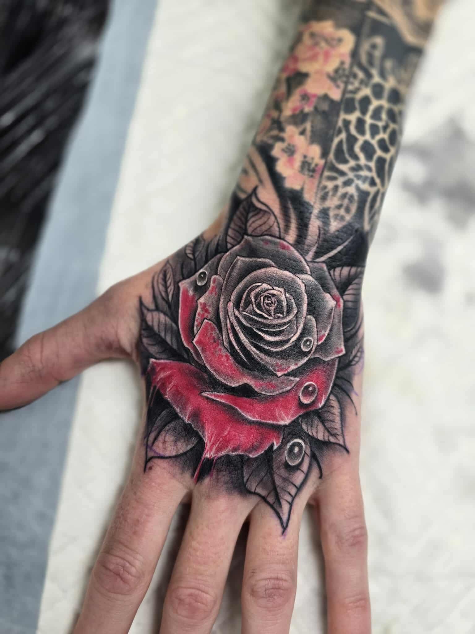 Hand Tattoo of a Red and Black Rose With Water Droplets, Leaves — Redback !nk Tattoo Studio in Kawana, QLD