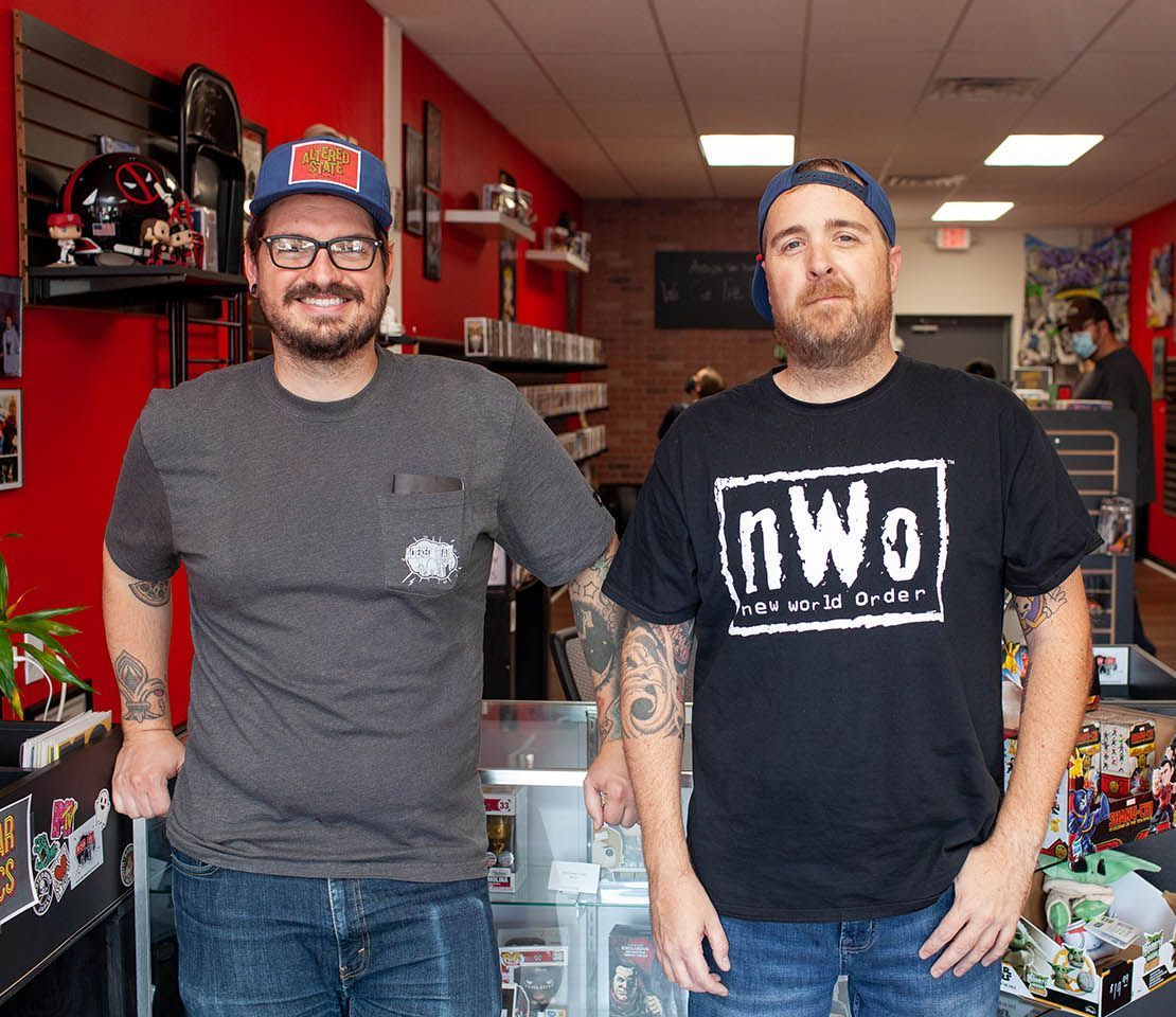 Two men in a store; one in a NWO shirt, one wearing a hat. Inside a game store.