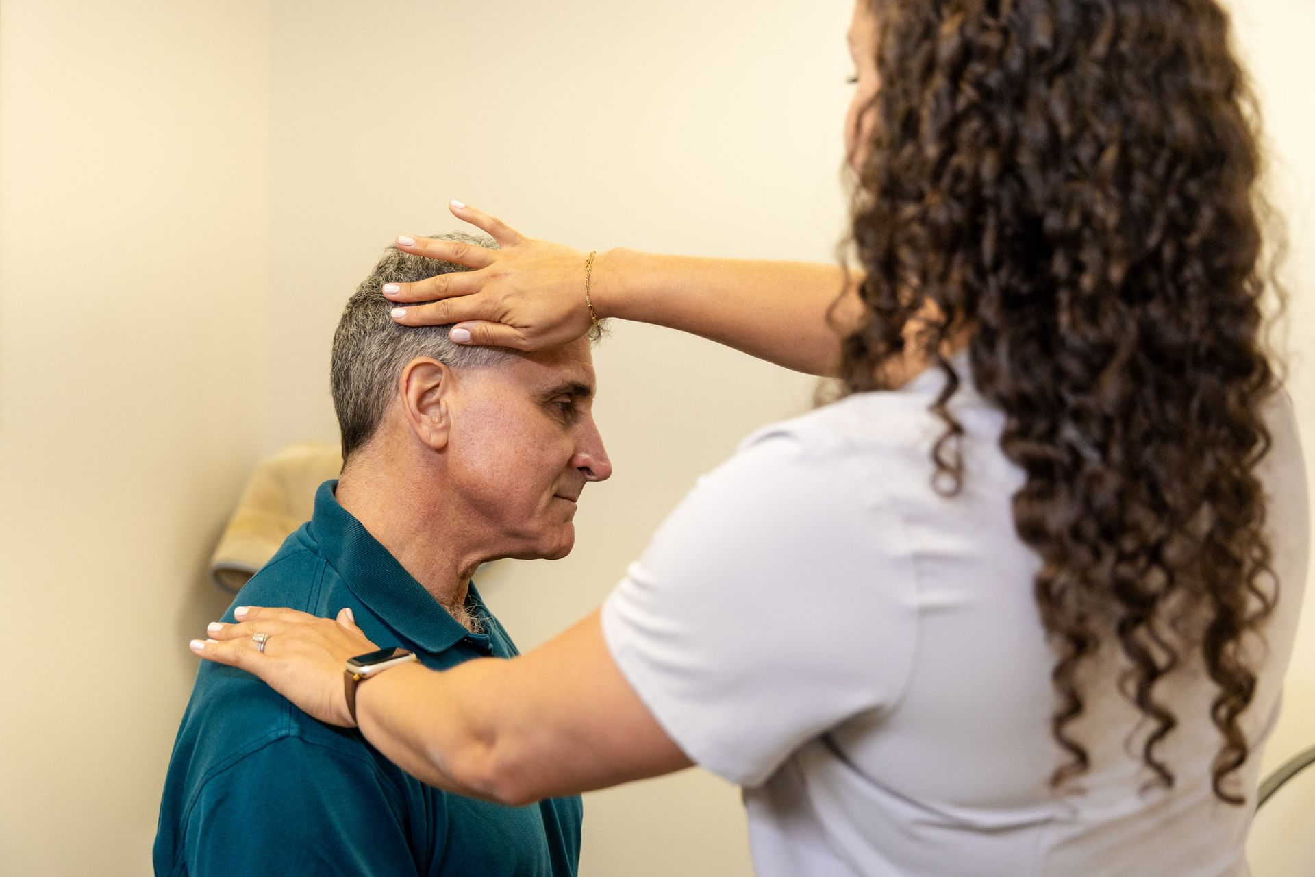 Dr. Cristal Laboy examining a person's head and shoulder. The provider wears light scrubs, patient wears a teal shirt.