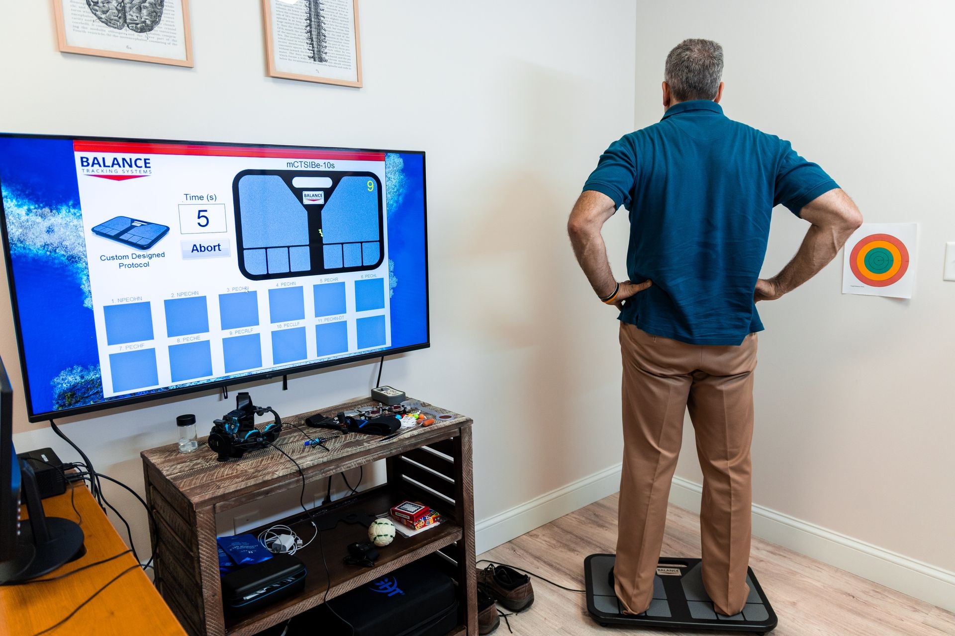 Man standing on a balance platform, looking at a screen. Testing or therapy room.