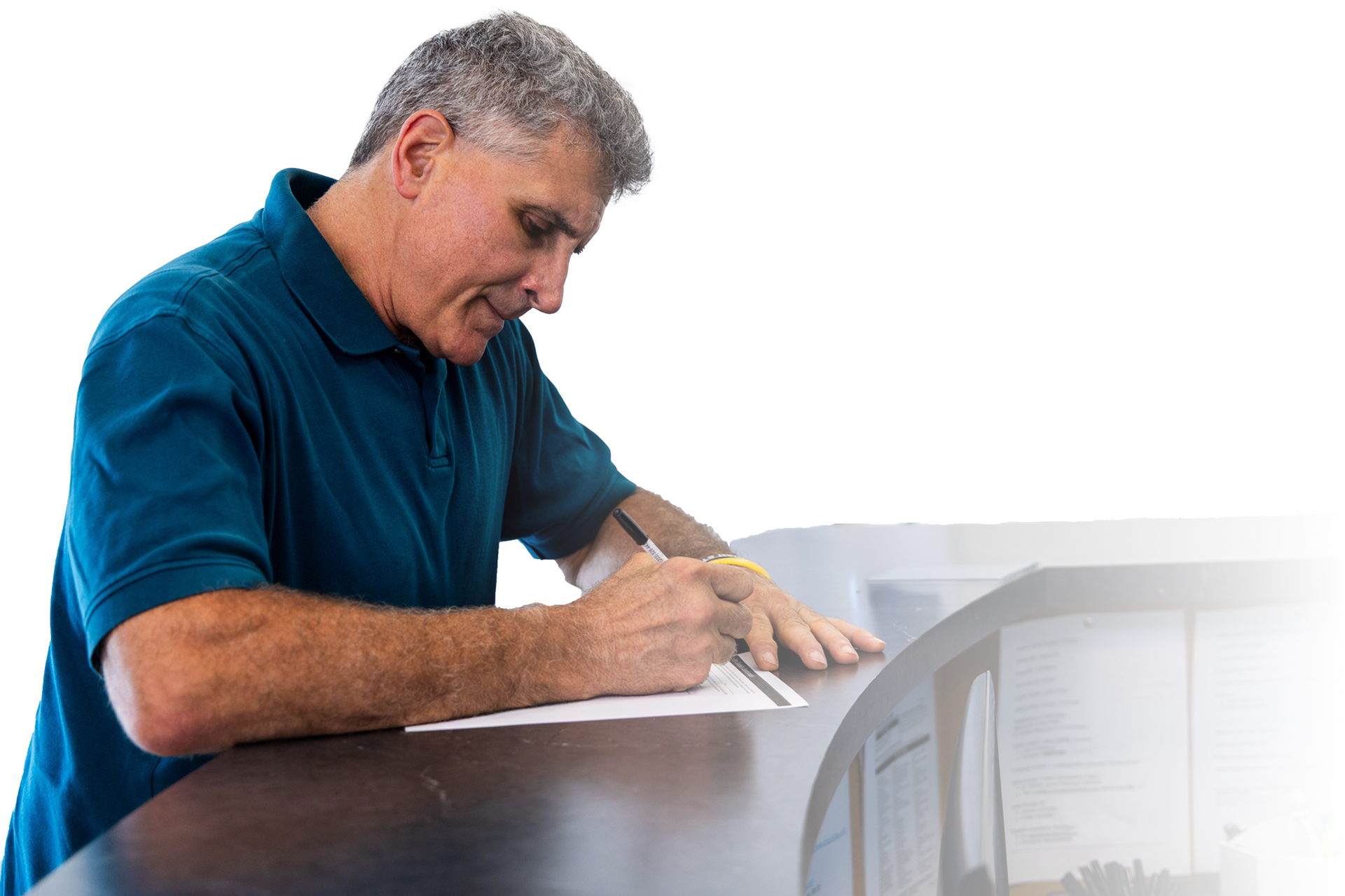 Man in blue shirt writing on paper at a counter.