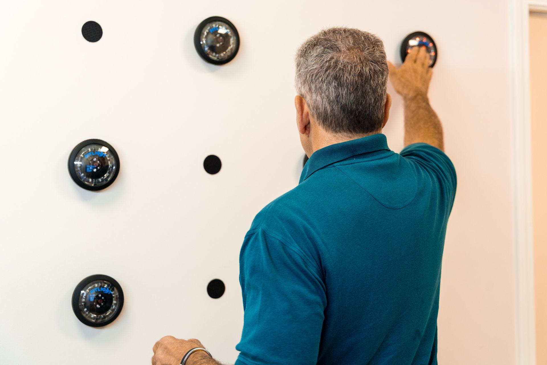 Man reaching up to adjust a round wall fixture on a white wall with other fixtures and black markers