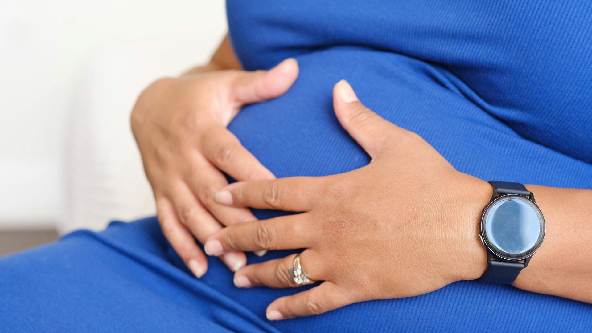 Hands cradling a pregnant belly, with a blue shirt and wristwatch visible